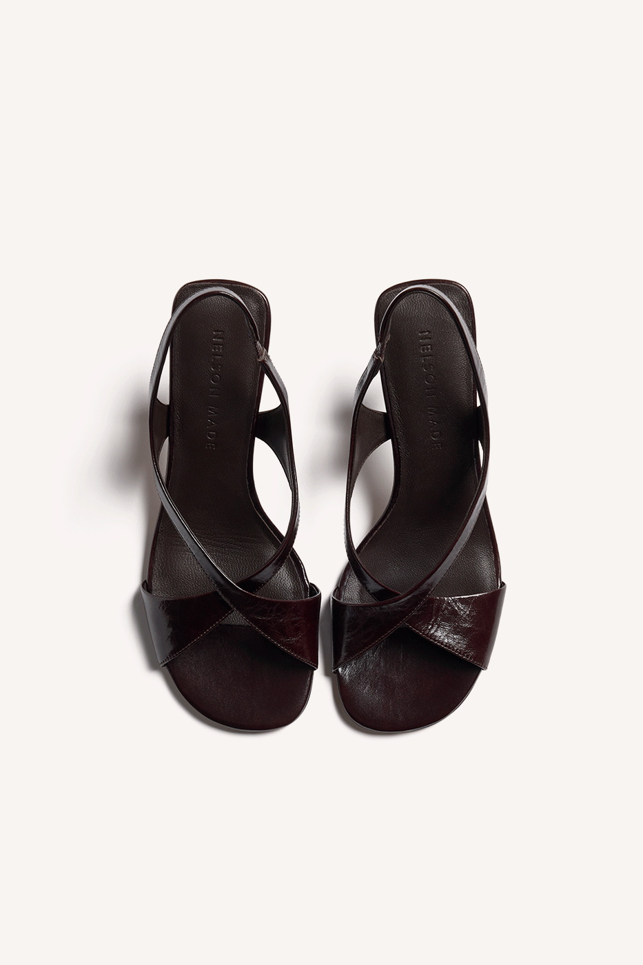 Nelson Made chocolate leather slingback sandals with criss-cross straps and a slim, set back heel, shown from a top angle view on a light beige background.