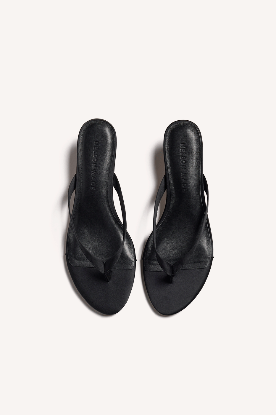 Nelson Made black satin thong sandals with thin strap and kitten heels, shown from a top view angle on a light off-white background.