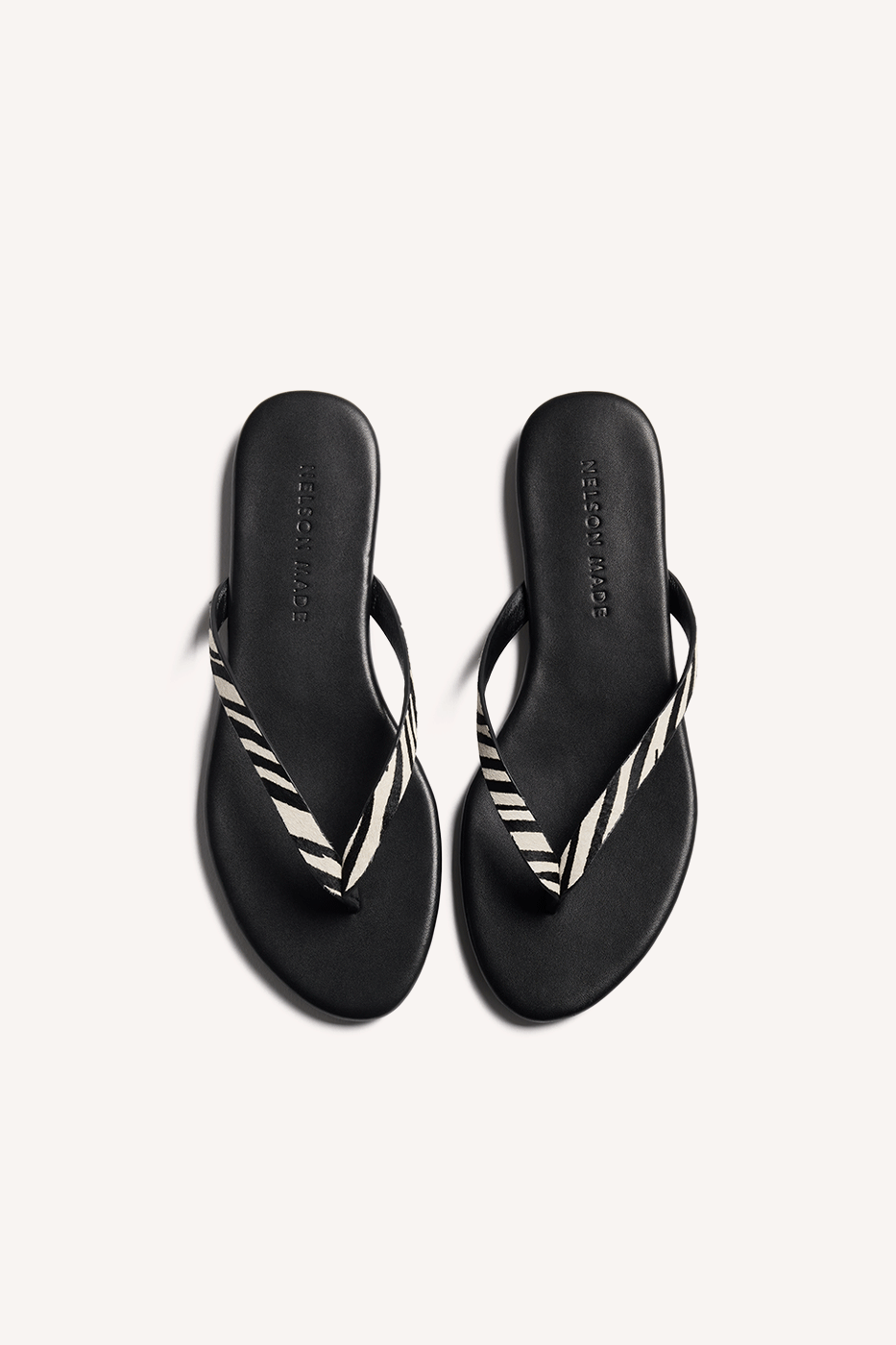 Nelson Made Zebra print thong sandals with a black leather sole shown from a top angle view on a light beige background.